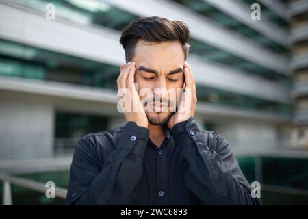Portrait of stressed middle eastern businessman suffering from headache outside Stock Photo