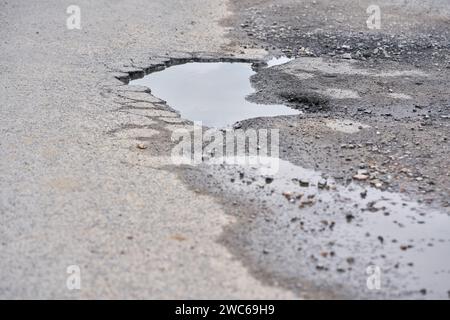 Pit on asphalt road filled with water. Stock Photo