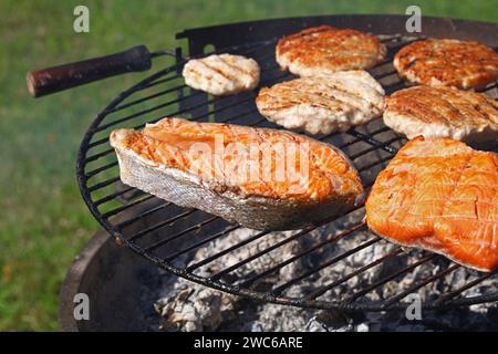 Close up chicken or turkey meat burgers for hamburger and salmon fish steak prepared on outdoor bbq grill, high angle view Stock Photo