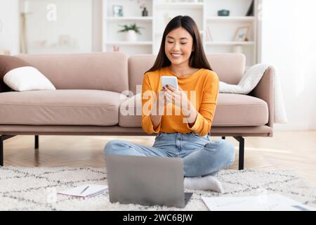 Pretty young asian lady entrepreneur using smartphone, home interior Stock Photo