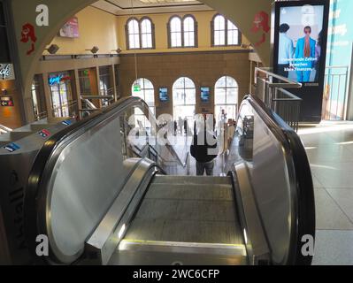 Looking down on escalator with man in train station building with old curved windows, travelers, large format bank advertisement with young woman Stock Photo