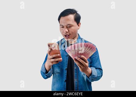 Young Asian man holding money and this phone showing excited expression when looking to his phone Stock Photo