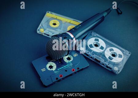 Black professional karaoke microphone and three colorful vintage audio cassettes on a black background. Dark blue toned photo with vignette. Stock Photo