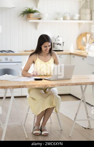 Positive woman sit at desk pay bills online on laptop Stock Photo