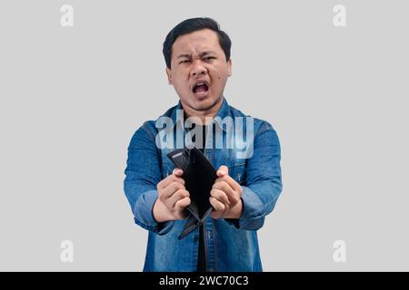 Young Asian man showing sad face expression while holding his empty wallet Stock Photo