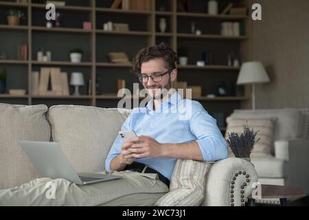 Smiling man rest on sofa with laptop and smartphone Stock Photo