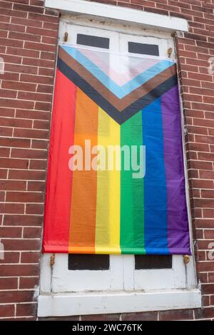 A vibrant rainbow flag is gracefully displayed on a windowsill, creating a striking contrast against the backdrop of a rustic brick wall Stock Photo