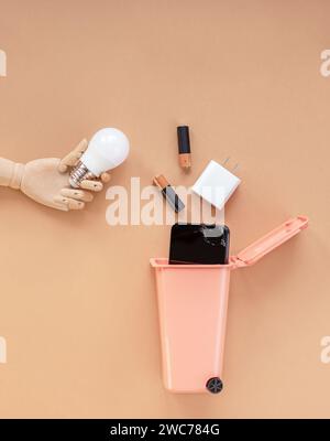 Wooden model of a hand holding a light bulb over a trash can. Garbage sorting concept. E-Waste disposal. Stock Photo