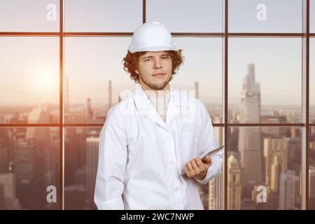Portrait of a young guy in white uniform holding tablet pc device. Indoor window with cityscape view in the background. Stock Photo