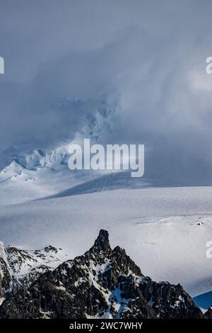 Elephant Island rocky shore and high snow-capped peaks, partially obscurred by lenticular and other clouds, Mount Pendragon, snow-capped peak, Stock Photo