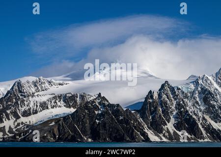 Elephant Island rocky shore and high snow-capped peaks, partially obscurred by lenticular and other clouds, Mount Pendragon, snow-capped peak, Stock Photo