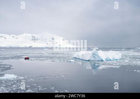 Zodiac navigating through the ice at Neko Harbor, Antarctica, ice filled water and icebergs grounded in place, reflections, and snow capped peaks Stock Photo
