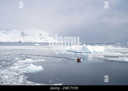 Zodiac navigating through the ice at Neko Harbor, Antarctica, ice filled water and icebergs grounded in place, reflections, and snow capped peaks Stock Photo