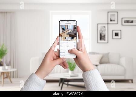 Woman's hands hold a smartphone in a living room interior. Using a luxury homes app to search for rent, blending modern technology with sophisticated Stock Photo