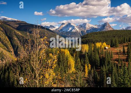 Mining shack nestled in aspens and pine forest beneath snow-covered mountains along the Million Dollar Highway in Colorado Stock Photo