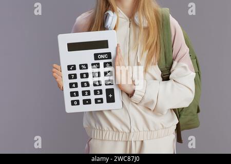 Closeup on school girl in beige tracksuit with backpack, calculator and headphones isolated on grey. Stock Photo