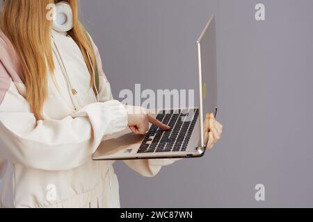 Closeup on teenager girl with headphones using laptop isolated on grey. Stock Photo