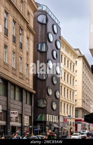 Vienna, AT - June 9, 2023 Tourists walking past the unconventional Hotel Topazz and Lamée, with it’s round cornered brown mosaic façade. Designed by B Stock Photo