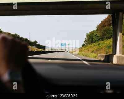 Captured from the driver perspective, this image showcases a clear day on the highway as we pass under a concrete overpass, with the journey stretching ahead - driving to Le Touquetm Boulogne, Calais in France - and to Berck too Stock Photo