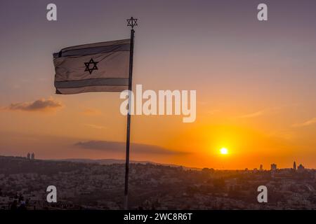 The Israeli flag (flag of Israel), the national symbol, is waving with the sun behind during the scenic sunset at Jerusalem. Stock Photo