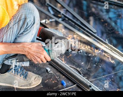 Worker cutting holders, aluminium profiles or aluminium structural frames using an electric grinder. Stock Photo