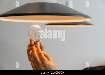 A young woman is changing a light bulb from an incandescent bulb to an LED bulb. Stock Photo