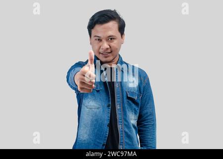 Young Asian Man showing thumb up in approval, recommending, like smth good, standing over white background Stock Photo