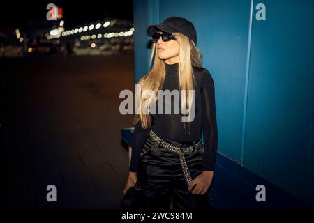 A Caucasian attractive woman in black grunge attire posing against a blue wall Stock Photo