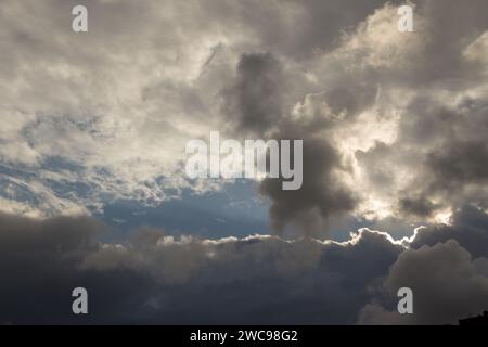 White and gray winter rain clouds with a background of blue sky. The sun trying to break through the clouds like an eye in the sky. Stock Photo