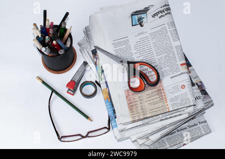 stacks of newspapers that need to be read to get information on business and financial news, plus stationery and glasses on the table Stock Photo