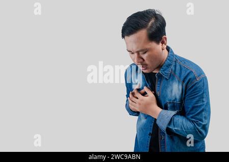Young Asian man having chest pain or heart trouble and pressing his chest on isolated white background. Stock Photo