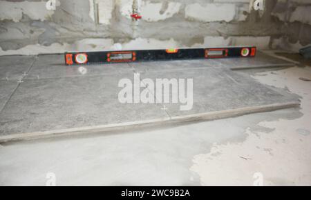 A close-up on large square natural stone, soap stone slip resistant bathroom tiles installation on a bathroom floor using a spirit level. Stock Photo