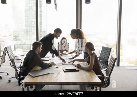 Multiethnic project colleagues discussing paper reports at meeting table Stock Photo