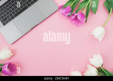 Laptop and tulips flowers on pink background. Flat lay. Top view. Female distant work concept. Stock Photo