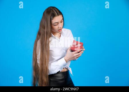 Astonished lady with long hair, opening mouth from surprise, while looking at small decorated box. Stock Photo