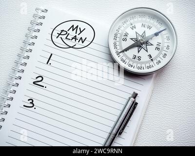 To do list. Handwritten text "MY PLAN" on the top of blank vertical notepad page with silver pen and compass on white spiral notebook. Business goals Stock Photo