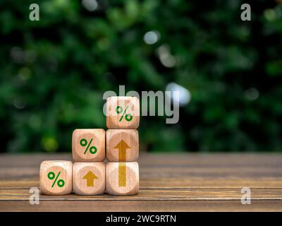 Green percentage and rise up arrows on wooden cube blocks as a business graph steps on table and green leaves background with copy space. Business gro Stock Photo