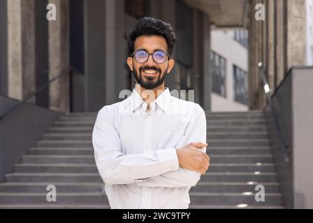 Confident young businessman with a beard smiling outdoors, dressed in a white shirt, expressing success and positivity. Stock Photo