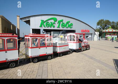 A kid's, children's toy train passes near the cable car, gondola top station. At the mountain top tourist amusement park area of Kok Tobe in Almaty, K Stock Photo