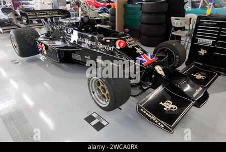 Three-quarters front view of a 1976, Black and Gold, Lotus 77, driven in period by Gunnar Nilsson, in the International Pit Garages at Silverstone Stock Photo