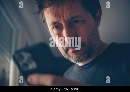 Surprised man looking at mobile phone text message recognizing sms scam and fraud activity. Smishing and spam activity. Selective focus. Stock Photo