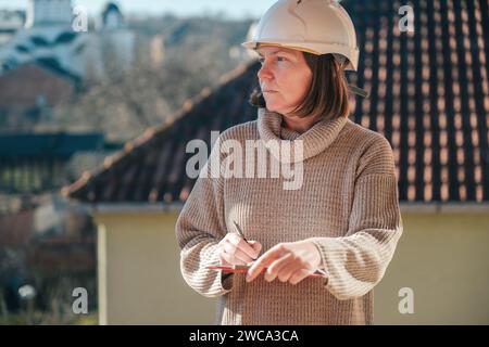 Female architect making notes and remarks during building site inspection, selective focus Stock Photo