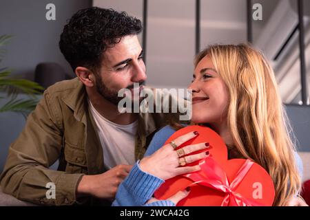 Young couple looking lovingly at each other with heart-shaped gift box. Valentine's Day Celebration. Stock Photo