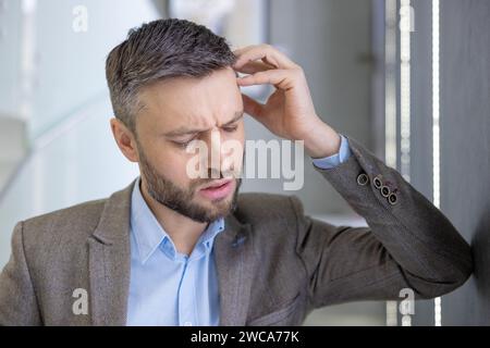 Confused businessman scratching head, expressing doubt and problem solving in a modern office setting, portraying perplexity. Stock Photo
