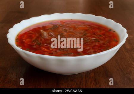 The image shows a white ceramic bowl of tomato soup placed on a wooden surface. The soup is red and appears chunky, with visible bits of vegetables an Stock Photo