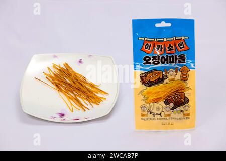 Ulsan, South Korea - January 14, 2024: A display of dried squid in long thin strips on a plate, alongside its original 'Squid Village' packaging, show Stock Photo