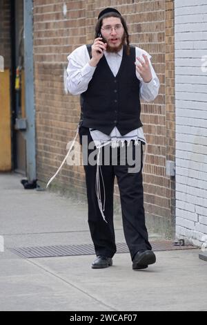 An orthodox jewish man talks on his flip phone while taking a brief brake from his job. In Brooklyn, New York Stock Photo