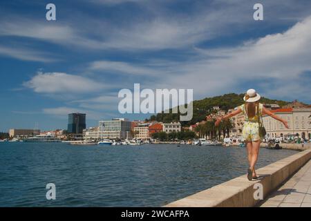 a young attractive woman in a hat walks along the waterfront in Split, Croatia Stock Photo