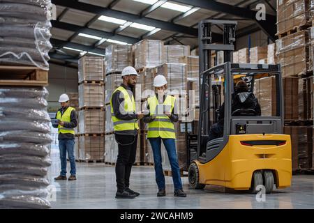 Warehouse workers reading product order, order picking. Warehouse manager checking delivery, stock in warehouse, inspecting products for shipment. Stock Photo