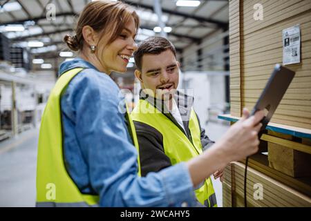 Young man with Down syndrome working in warehouse, female colleague teaching him scan products with scanner. Concept of workers with disabilities Stock Photo